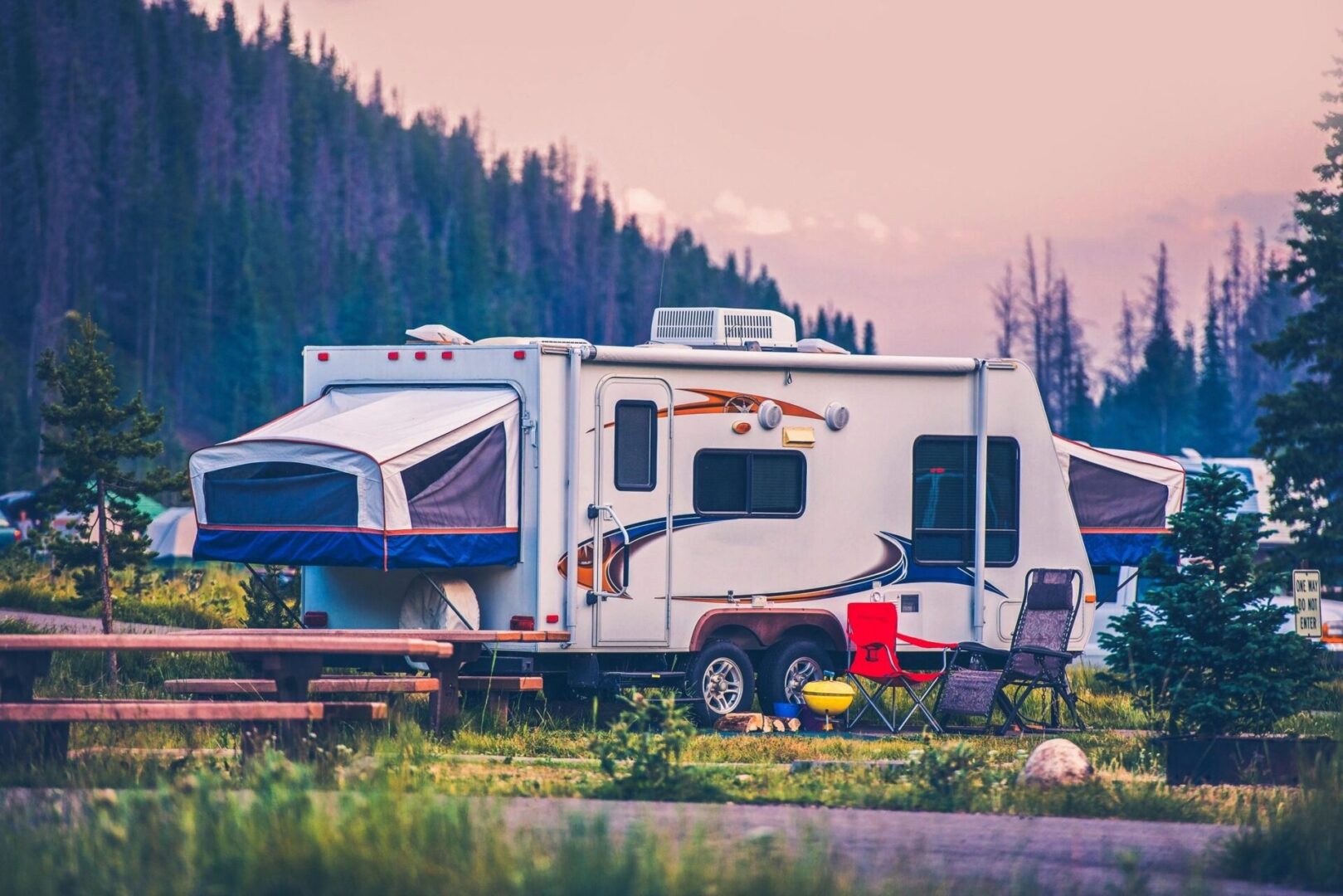A white camper parked in the grass near trees.